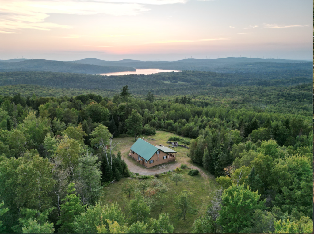 Aerial view of a camp in Northern Maine surrounded by trees and mountains, representing remote properties and cabins that may benefit from professional home inspections and radon testing.